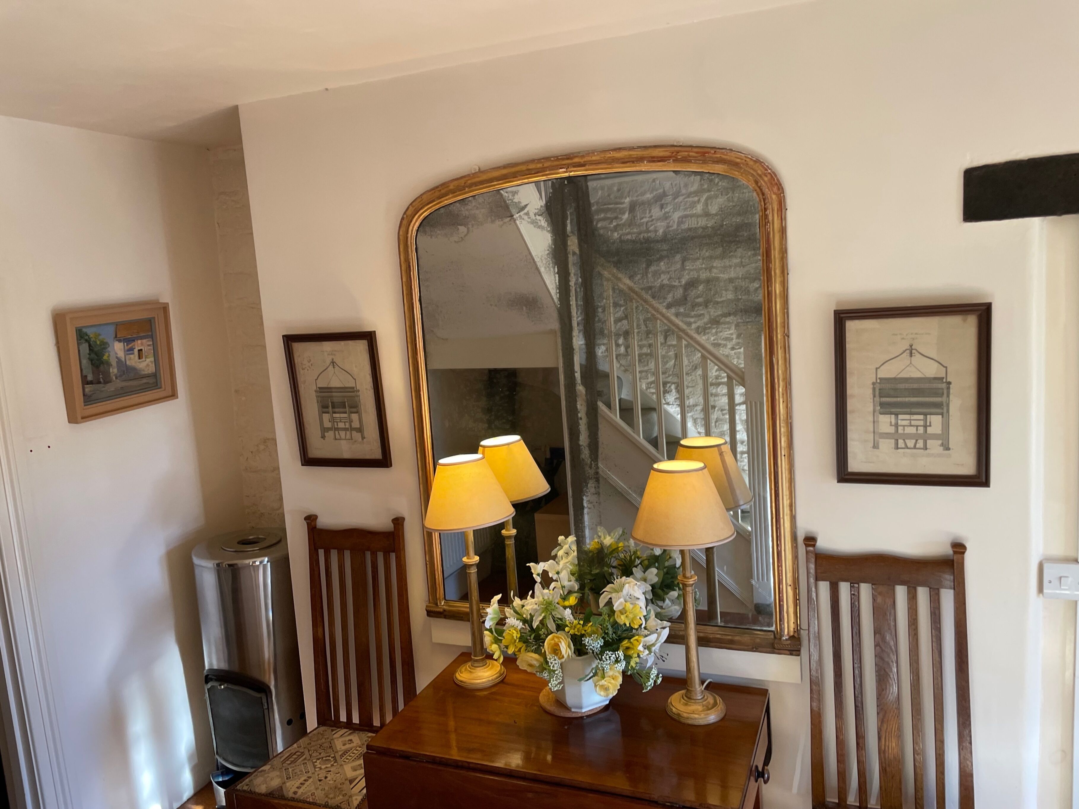 Une pièce avec une table en bois, deux lampes, un miroir et des tableaux encadrés accrochés au mur.