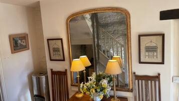 A room with a wooden table, two lamps, a mirror, and framed pictures on the wall.