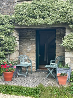 Une entrée en pierre, avec deux chaises vertes et des plantes en pot.
