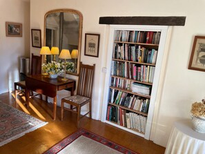 Un coin repas avec une table en bois, des chaises, un miroir et une bibliothèque remplie de livres.