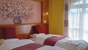 Habitación de hotel con dos camas, cabecero de madera, una obra de arte floral grande y una ventana con cortinas traslúcidas.