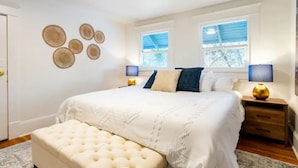 Een slaapkamer met een groot bed, twee nachtkastjes, een bankje en decoratieve muurkunst.