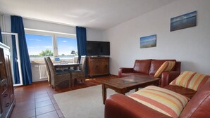 A living room with a sofa, a coffee table, a TV, and a dining area with chairs and a table.