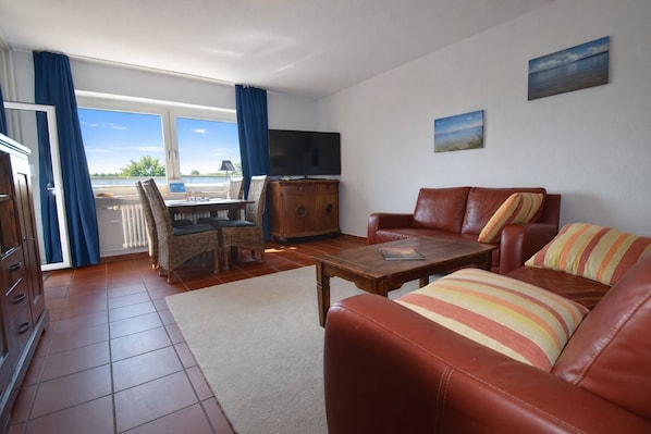 A living room with a sofa, a coffee table, a TV, and a dining area with chairs and a table.