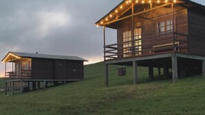 Una cabaña de madera con balcón, un edificio más pequeño adyacente y una colina cubierta de césped.