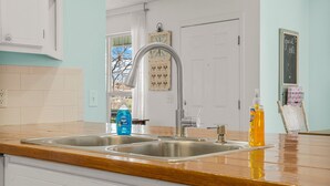 A kitchen with two stainless steel sinks, a wooden countertop, and a window with a view of trees.