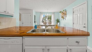 A kitchen with a wooden countertop, double sink, white cabinets, and a window with curtains.