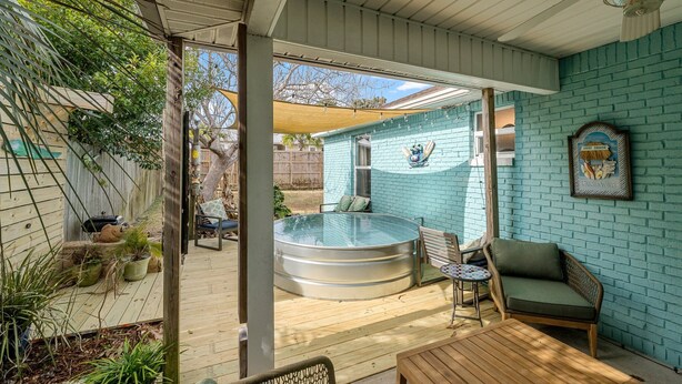 A covered patio with a hot tub, seating, and a brick wall.