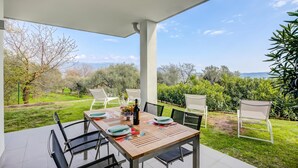 An outdoor dining area with a table set for four, surrounded by chairs, and a view of a grassy landscape with trees and hills. - Casa Oleandri Shared Pool & Lake View, Toscolano Maderno, Italy (Toscolano Maderno)