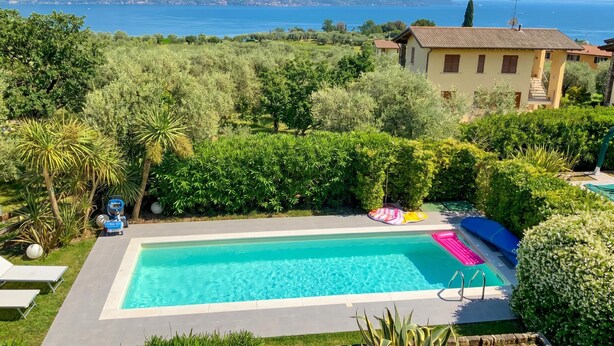 A swimming pool surrounded by lush greenery, with a view of the sea and mountains in the background. - Casa Oleandri Shared Pool & Lake View, Toscolano Maderno, Italy (Toscolano Maderno)