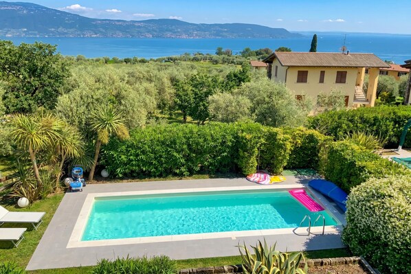 A swimming pool surrounded by lush greenery, with a view of the sea and mountains in the background.