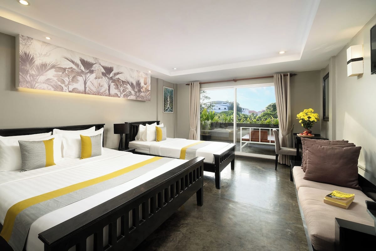 Een hotelkamer met twee bedden, een balkon met uitzicht en een zithoek met een tafel en stoelen.
