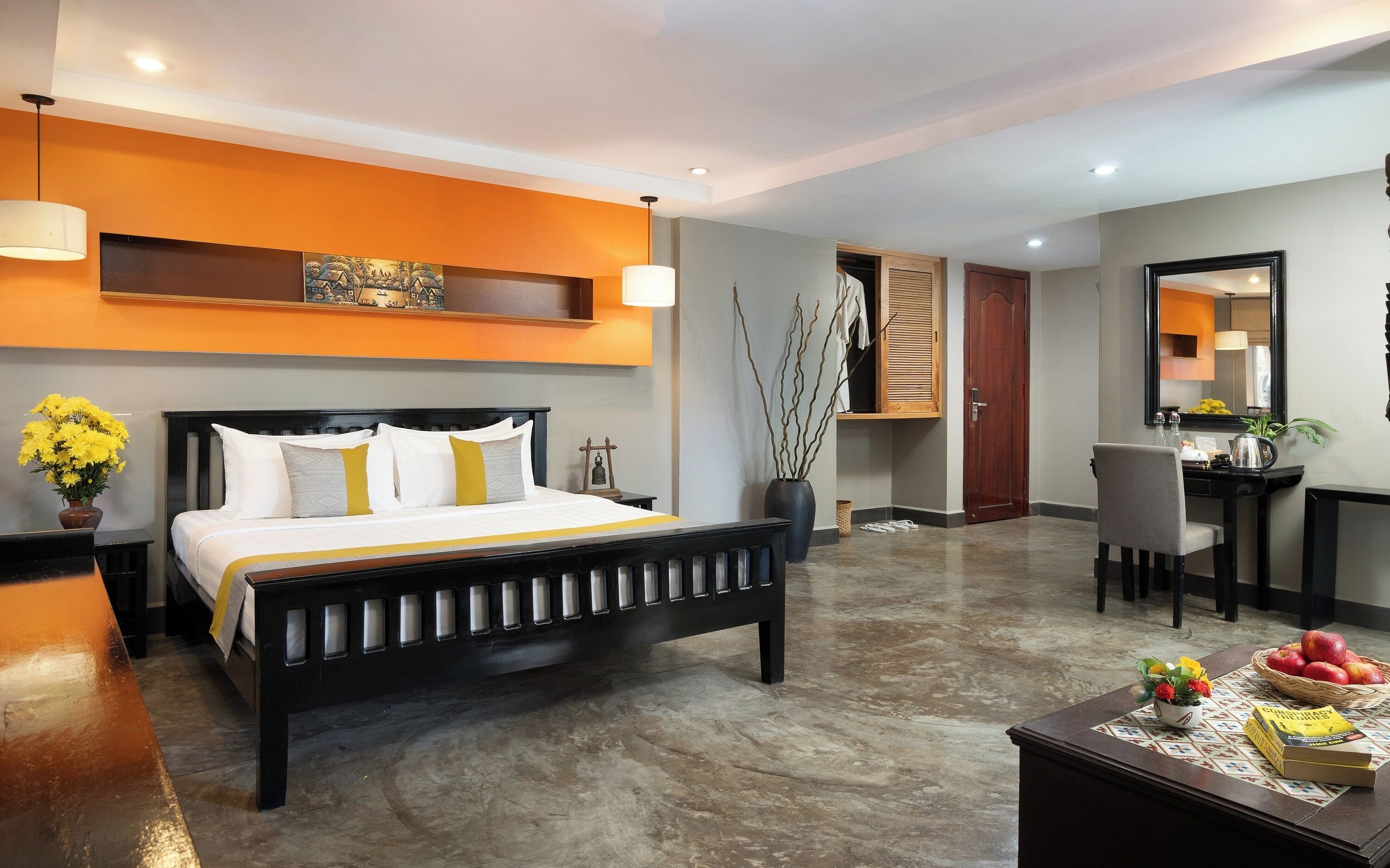 Habitación de hotel con cama, escritorio, silla, espejo y un florero con flores.