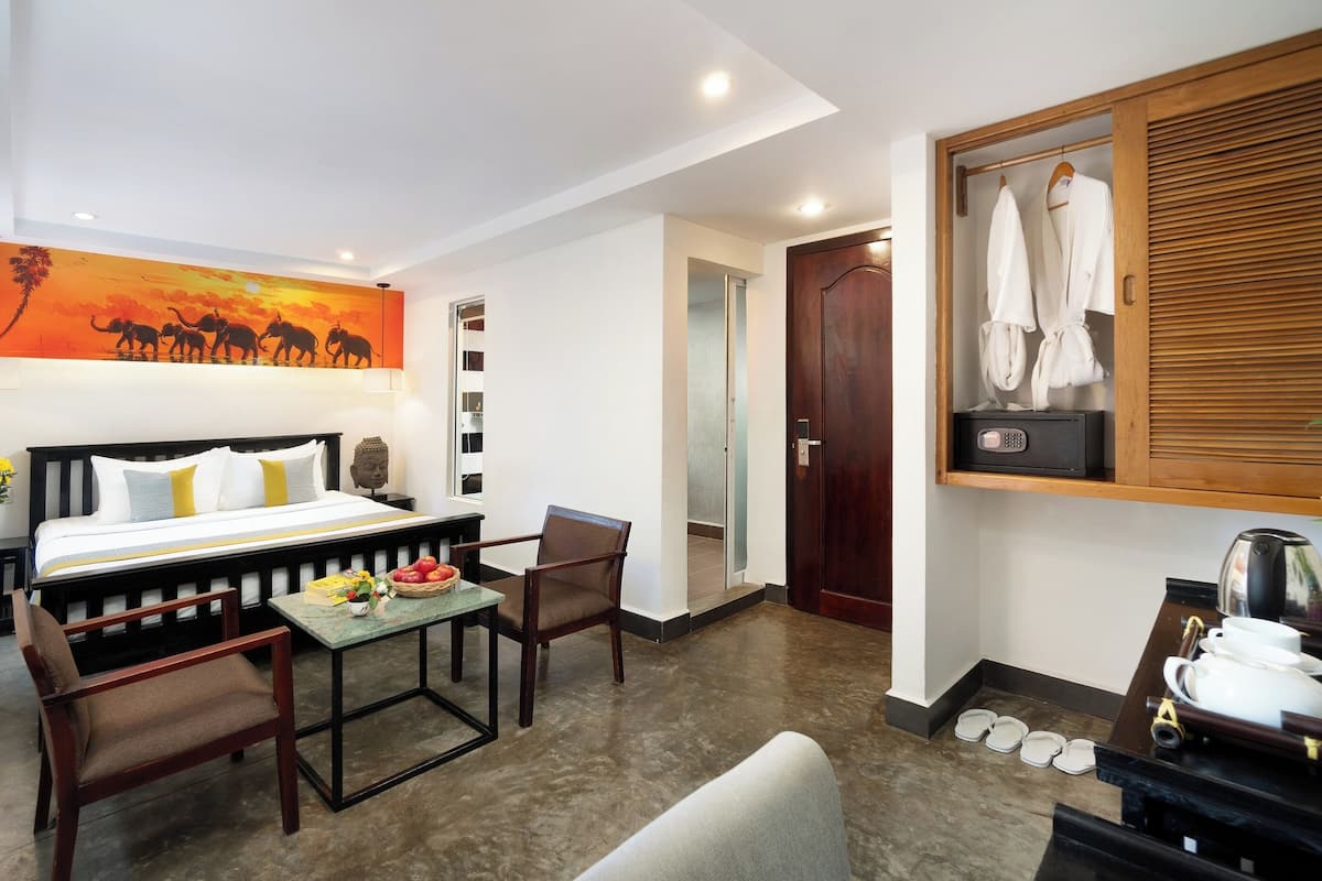 Een hotelkamer met een bed, een bureau, een stoel, een klein tafeltje met fruit, een schilderij en een kledingrek.