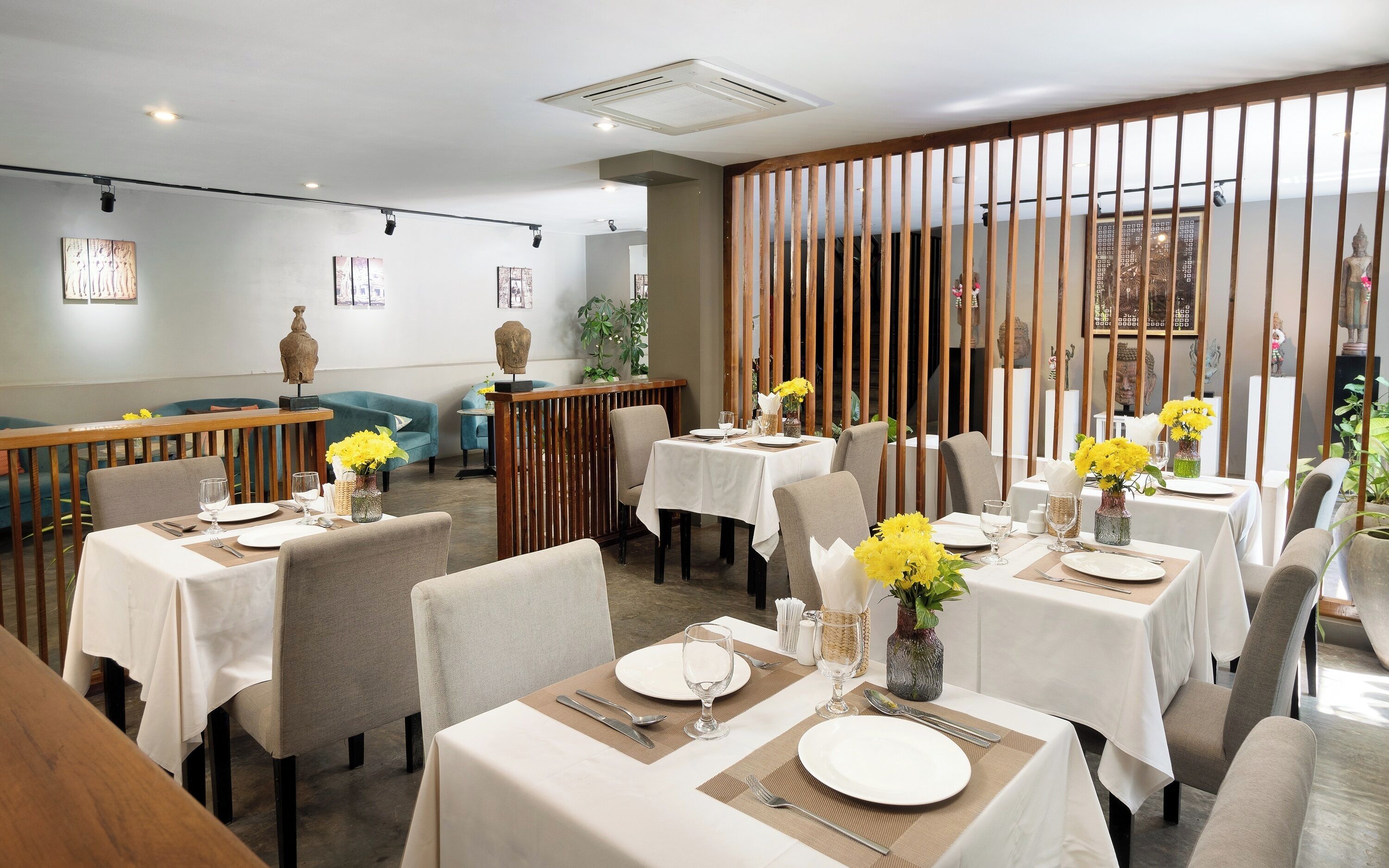 Ein Restaurant mit mehreren gedeckten Tischen, mit weißen Tischdecken und gelben Blumen.