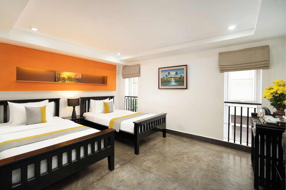 A hotel room with two beds, a window with a view, and a balcony with flowers.