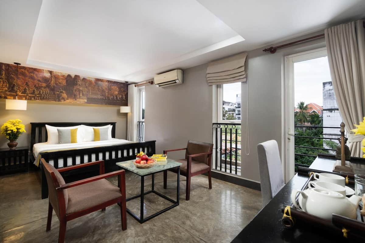 Hotelkamer met een bed, twee stoelen, een klein tafeltje, een balkon met een hekwerk en een raam met gordijnen.