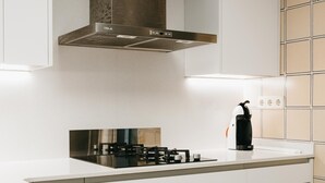 Una cocina moderna con armarios blancos, una campana extractora de acero inoxidable y un hervidor negro sobre la encimera.