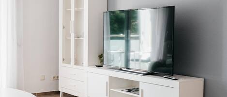 A modern living room with a white entertainment unit, a flat-screen TV, and a dining table.