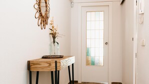 Un pasillo con una consola de madera, un jarrón con flores secas, un espejo decorativo y una puerta con panel de vidrio esmerilado.