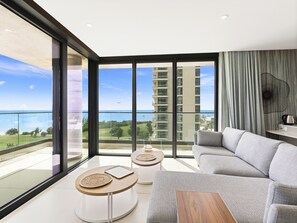 A modern living room with a grey sofa, two round tables with woven placemats, and a view of the ocean and a high-rise building. - B-702 Stunning ocean view (Cupecoy)