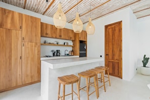 A modern kitchen with wooden cabinets, a central island with stools, and pendant lighting. - Alicante Villa by DH (Ubud)