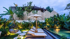 Un espace aménagé au bord de la piscine, avec des chaises longues, un fauteuil suspendu et une terrasse en bois.