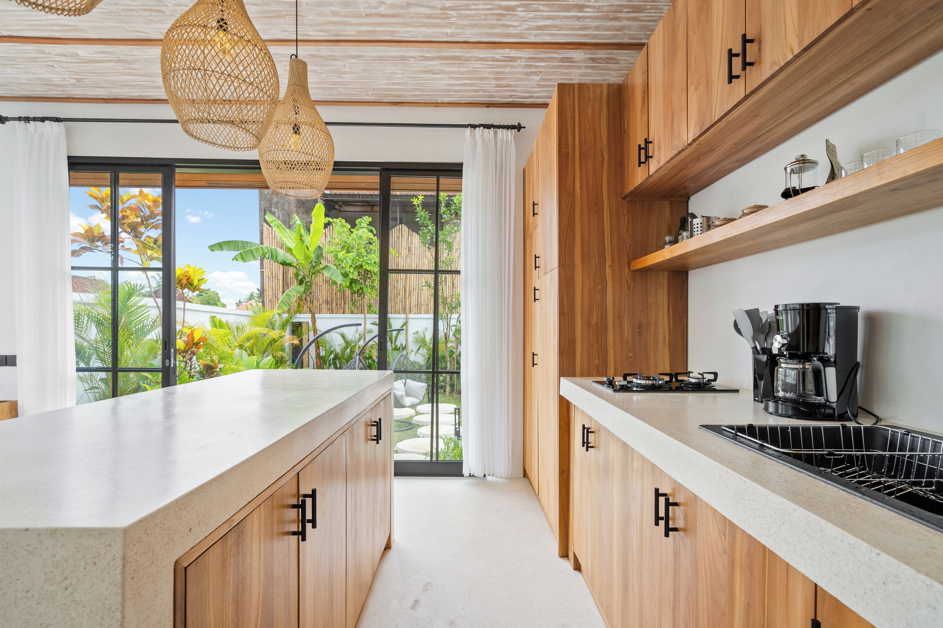 Eine moderne Küche mit Holzschränken, einer großen Kochinsel und Blick auf einen Garten durch Glastüren.