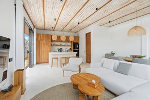 Een moderne woonruimte met een houten plafond, witte muren, een keukenhoek en een zithoek met een bank en stoelen.