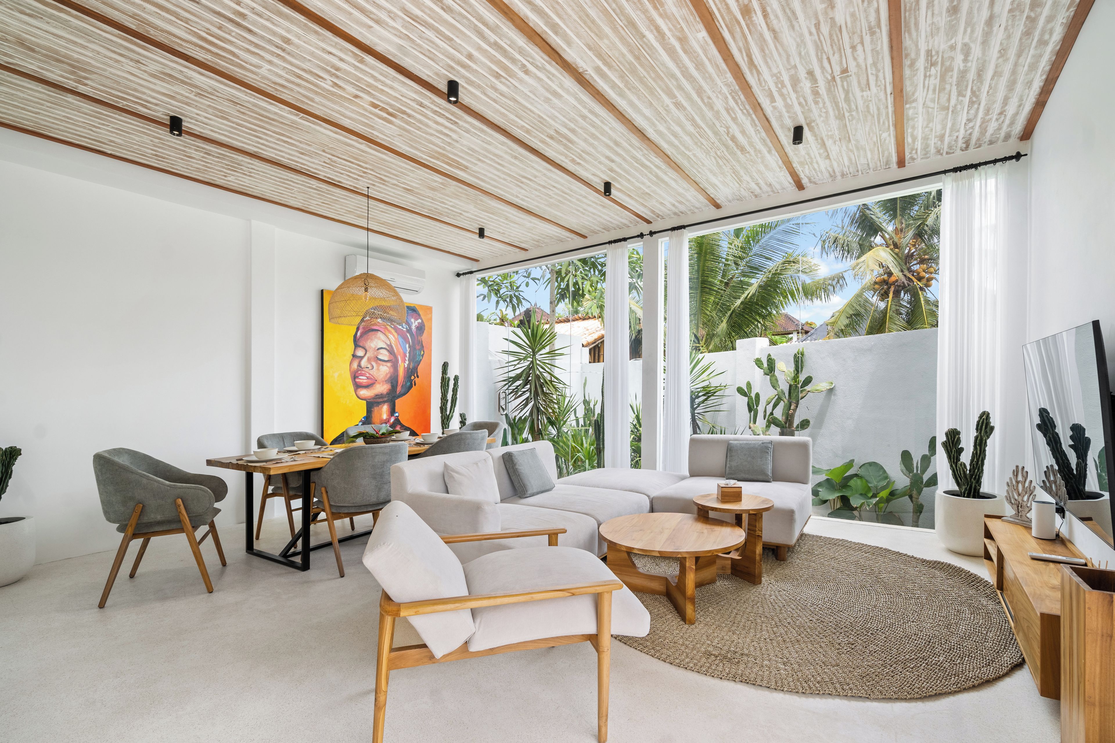 Una sala de estar moderna con un ventanal grande, un cuadro y una planta de cactus.