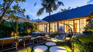 Un espace de détente extérieur moderne, avec des meubles en bois, un fauteuil suspendu et une piscine.