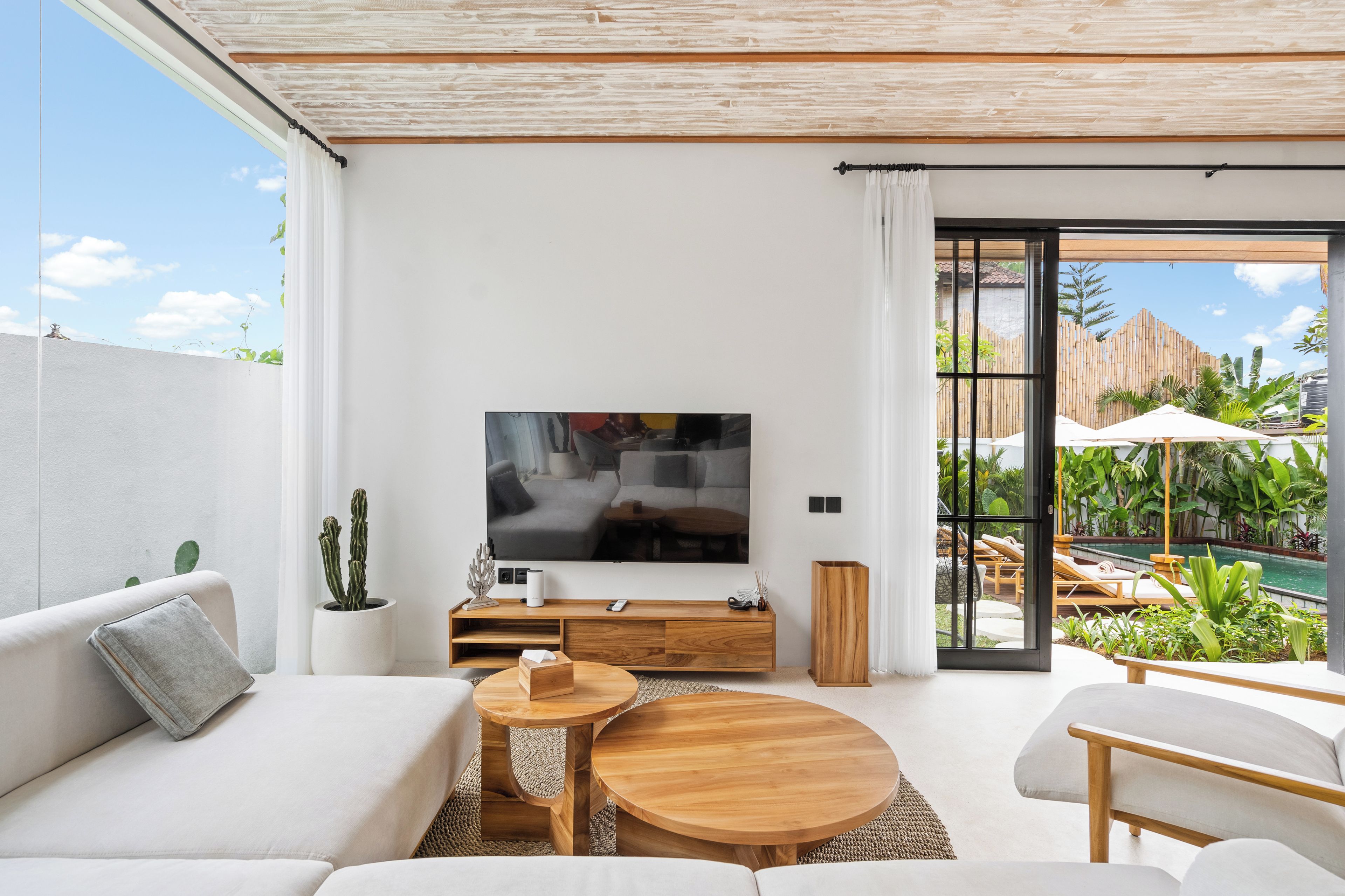 Sala moderna com televisão de tela plana, sofá, mesa de centro e vista para área de piscina externa.
