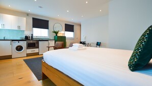 Ein modernes Hotelzimmer mit einem großen Bett, einer Waschmaschine, einer Mikrowelle und einer kleinen Küchenzeile.