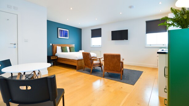 Ein modernes Hotelzimmer mit einem Bett, einem Esstisch, zwei Stühlen, einem kleinen Tisch und einem grünen Schrank.