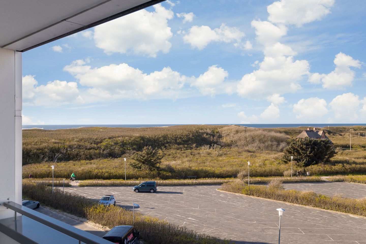 Ein Parkplatz mit Blick auf eine Küstenlandschaft, einschließlich einer Düne und eines Gebäudes mit Kegeldach.