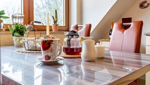 Un coin repas avec une table mise pour le thé, une chaise, une plante en pot et une fenêtre donnant sur des arbres.