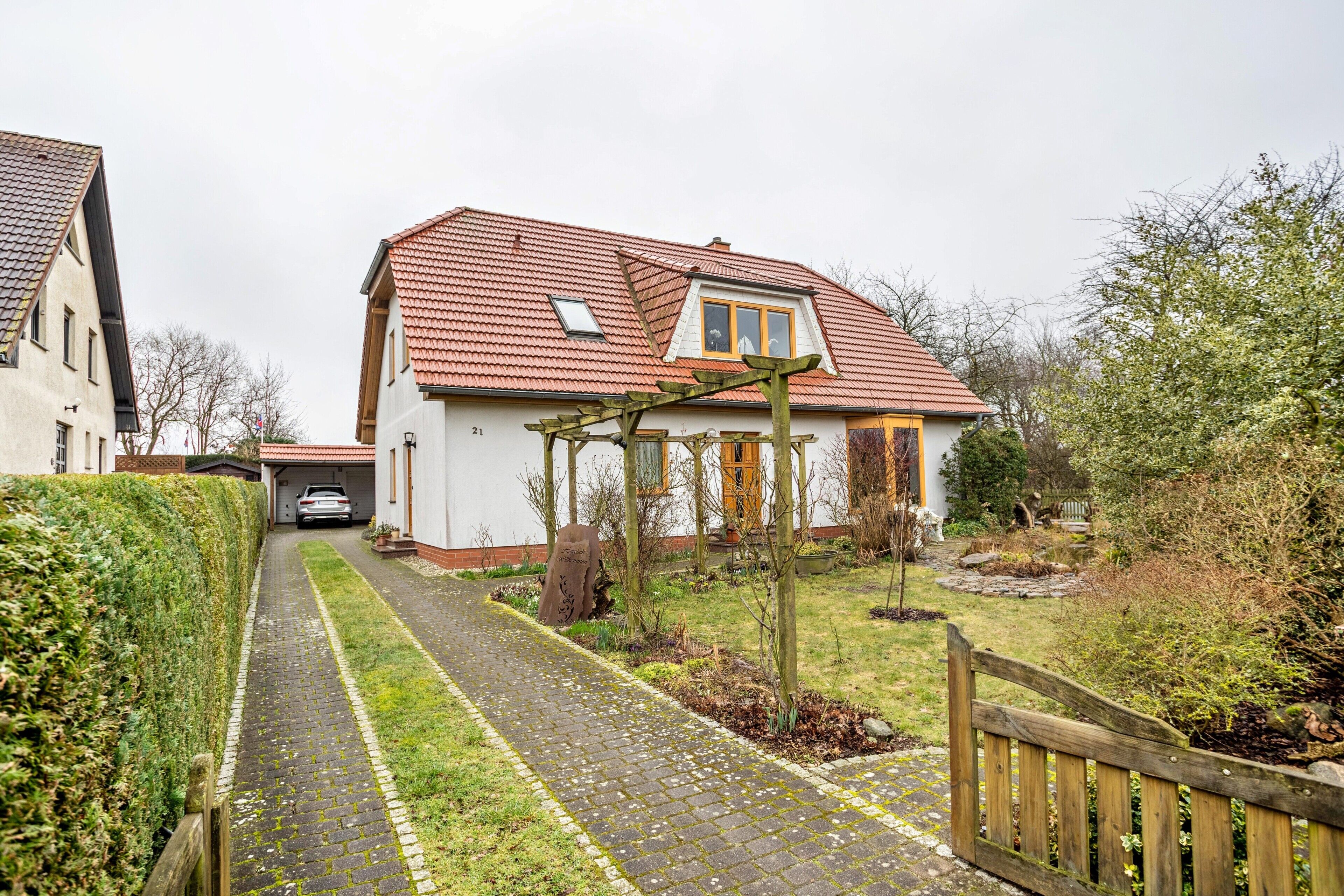 Ein Wohnhaus mit gepflasterter Auffahrt, einem Holztor und einem roten Ziegeldach.