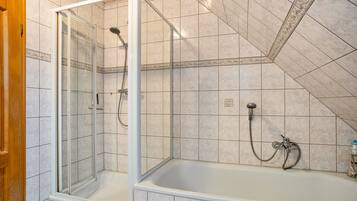Une salle de bain avec une douche à parois de verre, une baignoire et des murs carrelés.