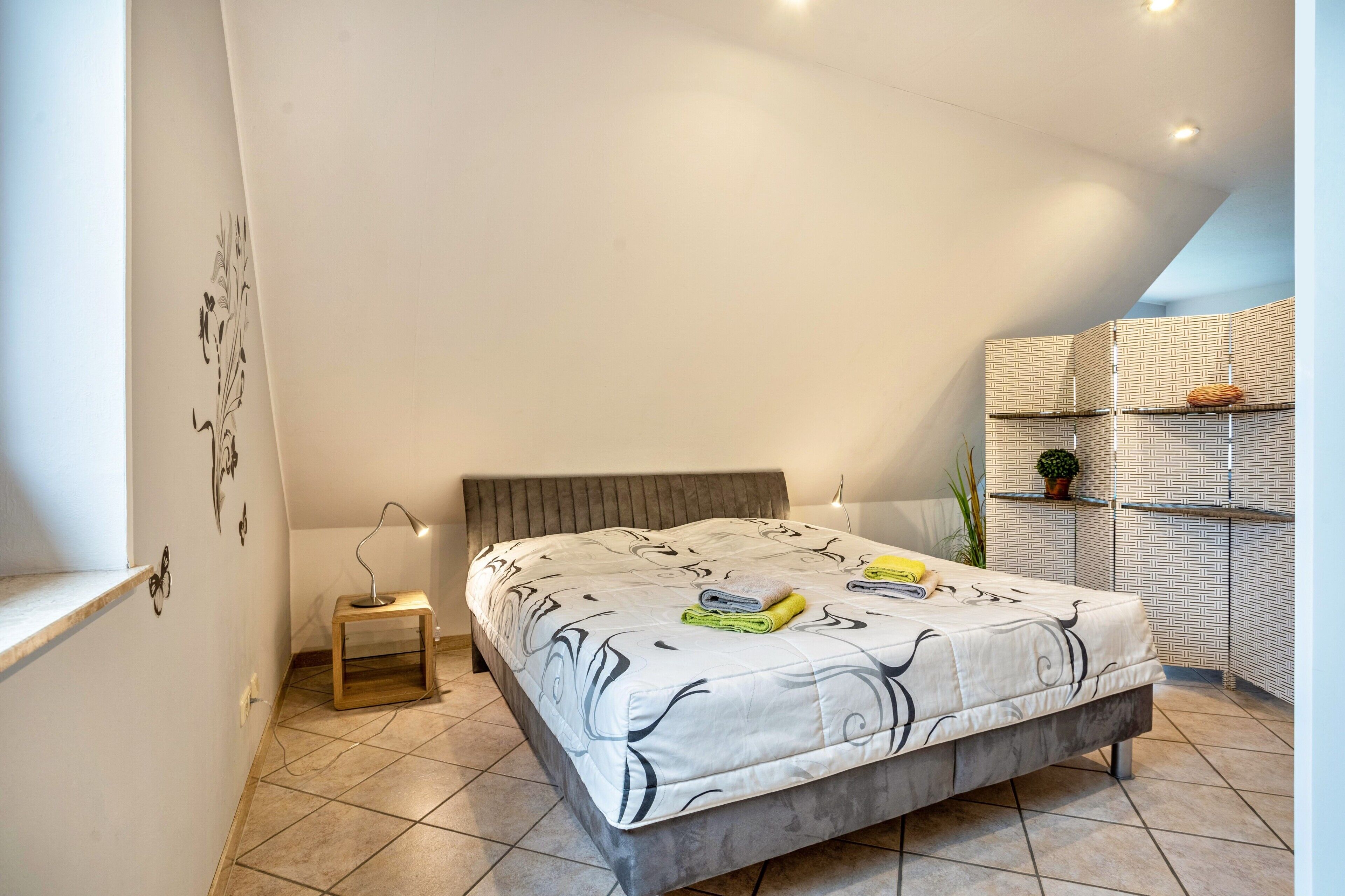 A bedroom with a bed, bedside table, lamp, and a wall with a geometric pattern.