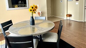 A dining area with a round table, black chairs, a vase with sunflowers, and a mirror on the wall.