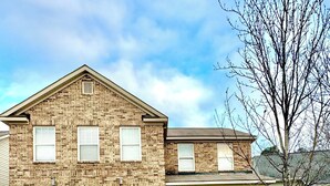 A two-story brick house with a garage, a covered porch, and a small tree in the front yard.