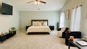 A bedroom with a bed, a desk, a chair, a ceiling fan, a TV, and a window with curtains.