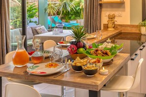 A dining table set with a variety of dishes, including rice, fried items, and a pineapple. There are also glasses, a pitcher, and a candle on the table. - Villa Idylle (ST LOUIS)