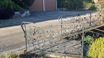 Eine Metallbank mit aufwendigen Verzierungen, ein gepflasterter Weg und ein Gebäude mit einer braunen Tür im Hintergrund.