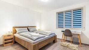 Une chambre à coucher avec un lit en bois, un bureau, une chaise, une table de chevet et une fenêtre avec des stores.