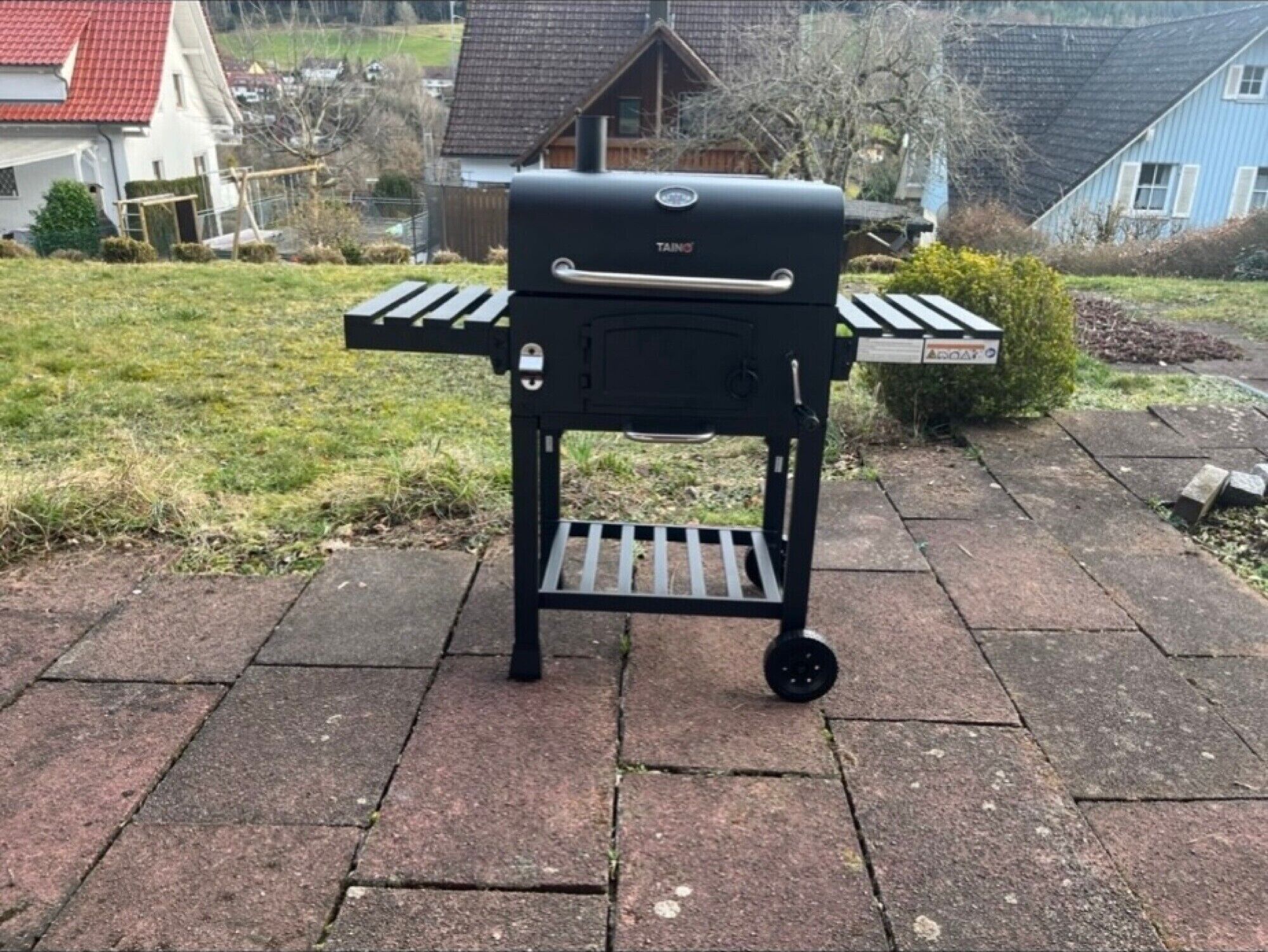 A portable barbecue grill with a handle and wheels, placed on a paved surface.