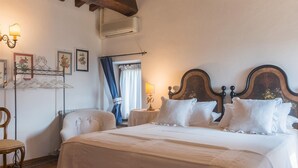 A bedroom with a large bed, wooden beams, a chair, a nightstand, and wall-mounted lights. - Casatorre 6 2 Emma Villas (Saludecio)