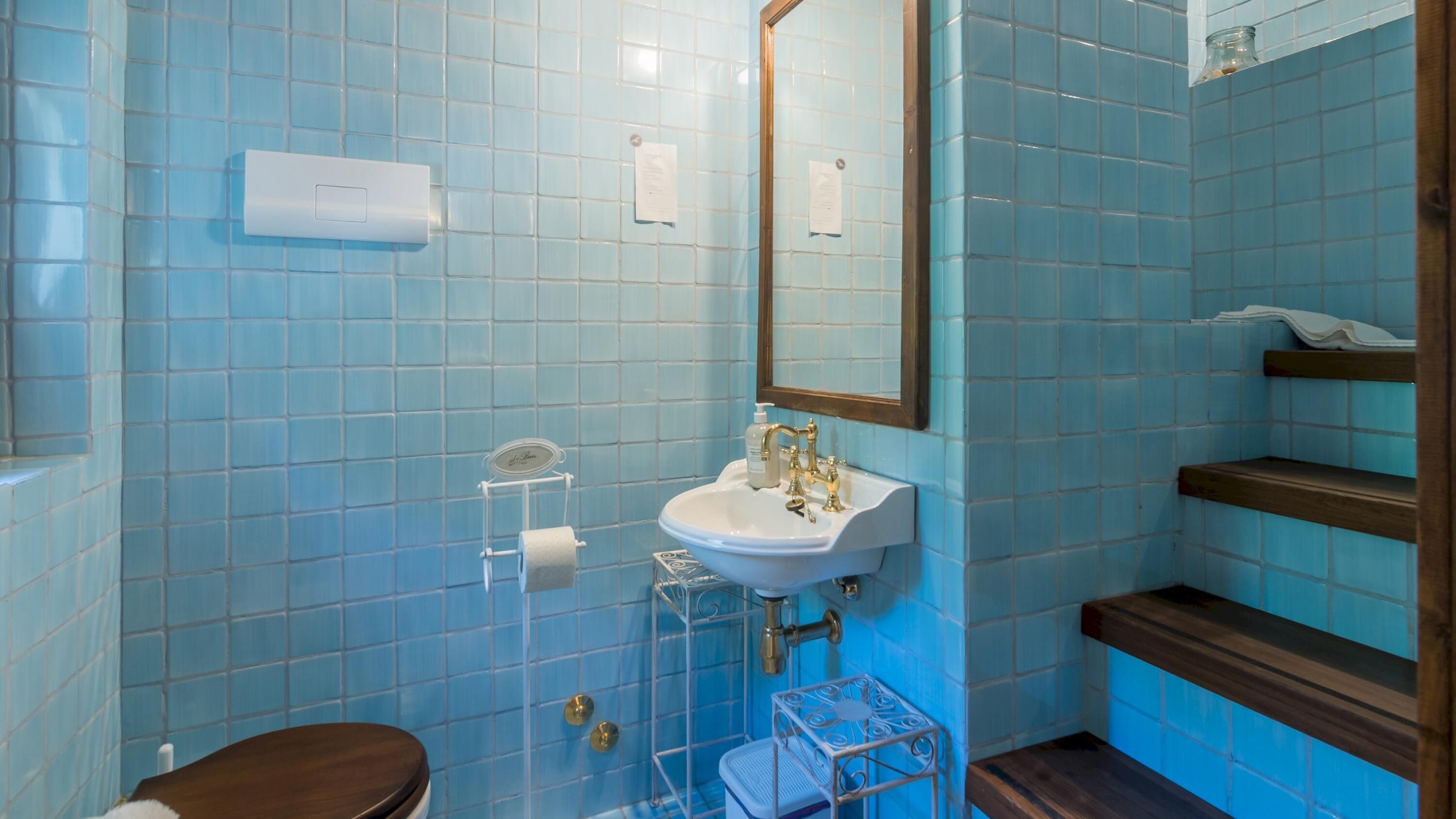 Ein Badezimmer mit blauen Fliesen, einem weißen Waschbecken, einem Spiegel, einer Toilette und einem Ablagebereich mit Handtüchern.