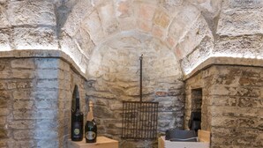 A stone-walled cellar with wooden crates containing wine bottles and boxes labeled "TENIMENTI GRIECO". - Casatorre 6 2 Emma Villas (Saludecio)