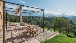 An outdoor patio with a pergola, seating, and a scenic view of rolling hills. - Casatorre 6 2 Emma Villas (Saludecio)